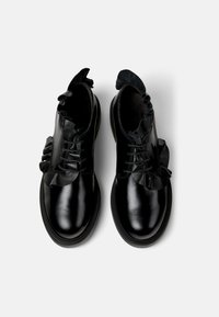 Zwarte leren schoenen met een glanzende afwerking, voorzien van een geplooide suède rand rond de veters en een afgeronde neus. Platte rubberen zool.