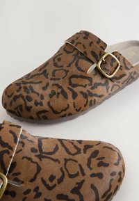Sabots marron à enfiler en fausse fourrure texturée avec un motif léopard, dotés d'une sangle à boucle et d'une semelle intérieure rembourrée.