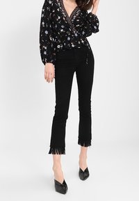 Blusa avvolgente nera con fiori, maniche a palloncino, scollatura a V e dettagli intricati, abbinata a jeans neri a vita alta con orlo frangiato e tacchi a punta.