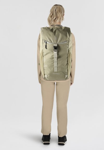 Zaino verde oliva con pattina superiore, spallaccio regolabile e tasche laterali. Materiale testurizzato con un logo nella parte anteriore inferiore.