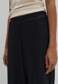 Pantalons noirs à jambe large en tissu lisse avec une taille haute. Présente des plis subtils et une apparence élégante et soignée.