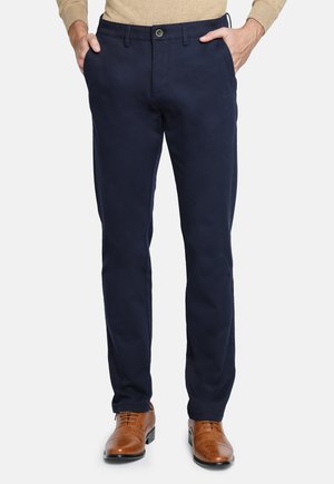 Chinos navy de mezcla de algodón, con cierre de botón, bolsillos delanteros y diseño de pierna recta, combinados con zapatos de cuero marrón.