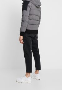 Grå pufferjacka med svarta axelaccenter, tillsammans med svarta smala jeans och vita sneakers. Har en huva och ribbad muddar.