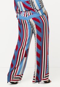 Pantaloni lunghi con un motivo a zig-zag in strisce blu, rosse, nere e bianche. Realizzati in tessuto morbido con una vestibilità rilassata.