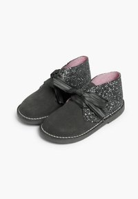 Botas de tobillo de ante negro con una parte superior brillante, que cuenta con un lazo de satén ancho. Suela texturizada y forro interior rosa.