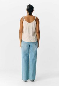 Haut sans manches beige clair avec des bretelles à nouer associé à un jean léger bleu clair ; texture de tissu lisse avec des détails de design minimalistes.