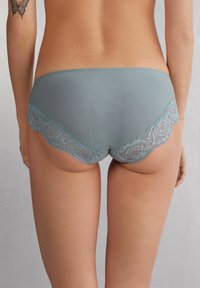 Blauwe panties met kant en een gladde stofafwerking, voorzien van een bloemenkantaccent langs de tailleband. Achteraanzicht dat het ontwerp toont.
