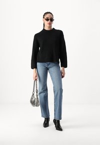 Juodas megztinis, mėlyni tiesaus silueto džinsai, juodi aukštakulniai auliniai batai, sidabrinė rankinė, katės akies formos saulės akiniai. Paprastas, modernus dizainas.