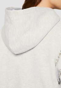 Grauer Hoodie mit weicher Textur, einer großen Kapuze und funkelnden Verzierungen an der Seite für zusätzliche Details.
