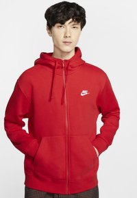 Rode zip-up hoodie van zacht materiaal, met een kangoeroe zak en een klein wit Nike logo op de linkerborst. Capuchon met aangehechte koordjes.