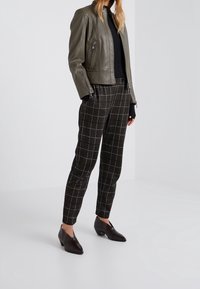 Oliivinvihreä nahkatakki, musta neule, tumman sävyisiä ruudullisia räätälöityjä housuja ja mustat korkeat nilkkasaappaat, joissa on teksturoitu pinta.