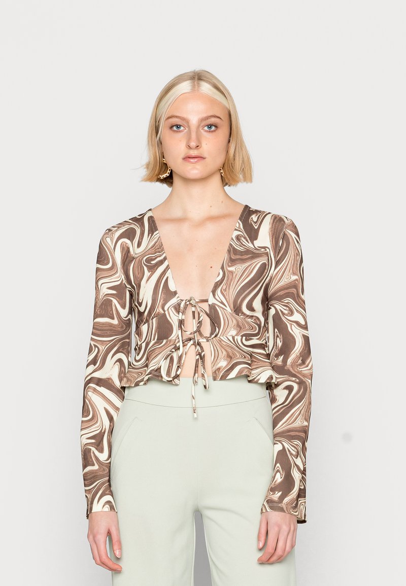 Top curto com padrão em espiral marrom e creme, decote em V profundo e frente amarrada; mangas longas e tecido leve.