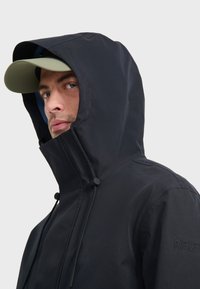 Sort vandtæt jakke med h�øj krave og justerbare snore, som har hætte og logo-broderi på skulderen.