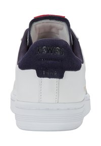 Zapatilla blanca con acentos de ante azul marino en el talón, lengua texturizada y detalle de logo dorado. Presenta una suela plana de goma blanca.