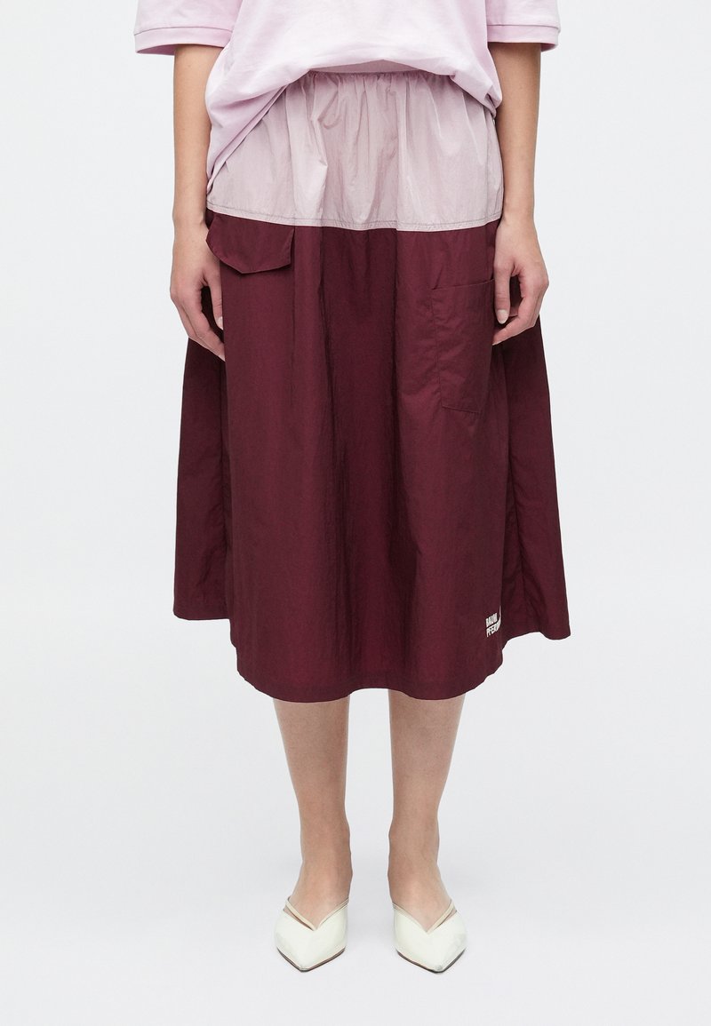 Μπορντό, φούστα μεσαίου μήκους με σούρα στη μέση, που διαθέτει διάφανο, κρεμ επικάλυμμα και πλαϊνές τσέπες. Λογότυπο κοντά στο τελείωμα.