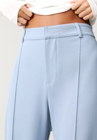Himmelblaue, maßgeschneiderte Hosen mit glatter Textur, schmaler Passform und vorderen Taschen mit präzisen Nähten sowie einem flachen Bund.