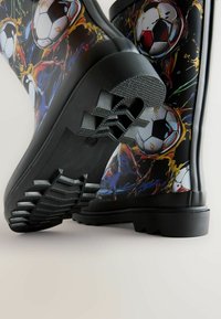 Black rubber rain boots featuring a colorful soccer ball pattern, textured soles, and a sturdy design, ideal for wet conditions.