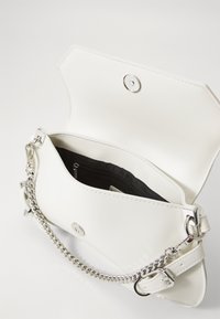 Witte neplederen handtas met een zilveren kettinghengsel, magneetsluiting en een zwarte gevoerde binnenzak voor organisatie.