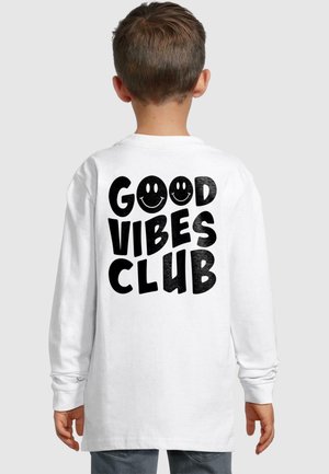 Pikad varrukad valge särk, mille seljal on suur must tekst "GOOD VIBES CLUB", mille kõrval naeratavate nägude aktsendid. Puuvillane kangas.