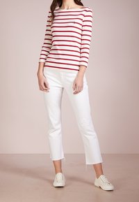 Frau, die ein weißes und rotes gestreiftes Langarmshirt, weiße verkürzte Jeans mit fransigen Säumen und weiße Schn�ürsneaker trägt.