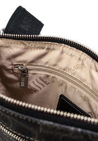 L'interno della borsa di stoffa nera presenta una tasca con zip, una fodera beige liscia con loghi e denti della zip e tirazip in metallo argentato.