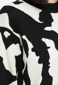 Zwart-wit trui met een abstract patroon, gebreide textuur, ronde halslijn en lange mouwen. Het ontwerp is gedurfd en contrasterend.