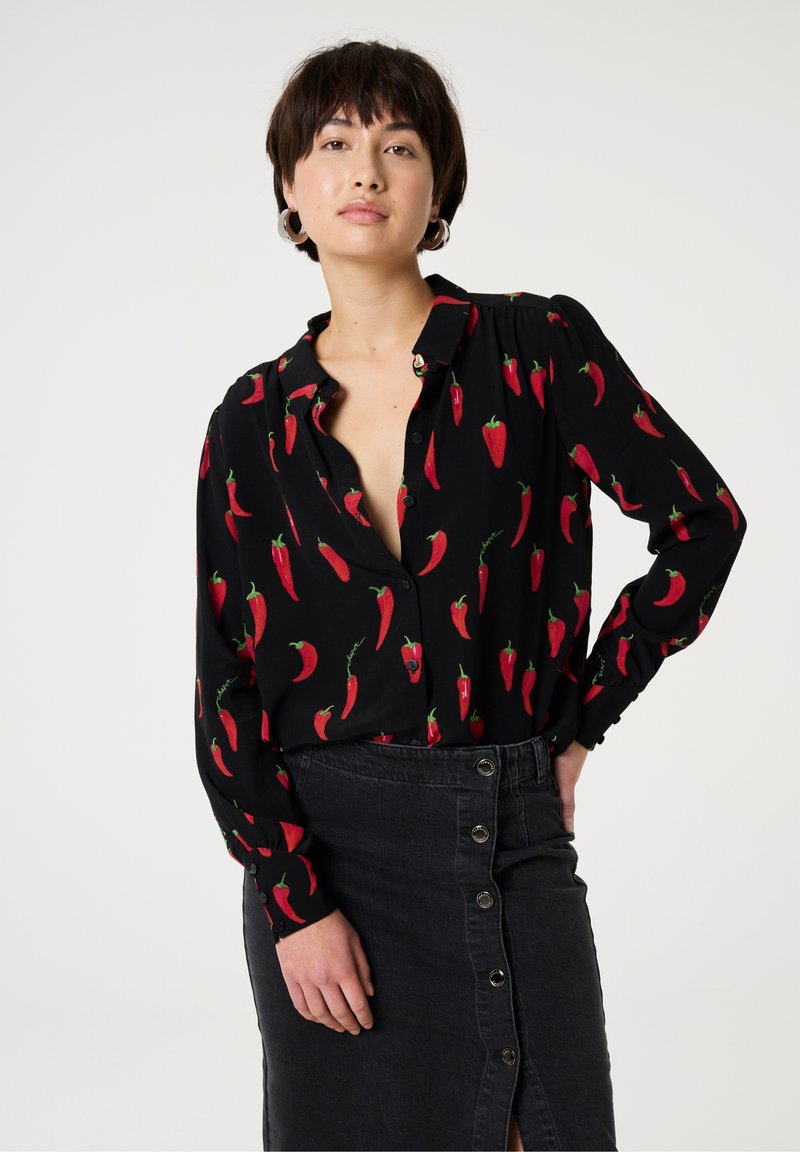 Black blouse with red chili pepper pattern, long sleeves, button-up front, and slightly loose fit. Paired with a black denim skirt featuring buttons.