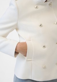Biseleur witte blazer in textuurstof met glanzende zilveren knopen en een zijzak, met een iets gestructureerde pasvorm.