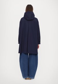Tums zils mēteli ar kapuci un pagarinātu aizmuguri, ar pogām pie aproces. Apvienots ar plašām zilo denimu biksēm.