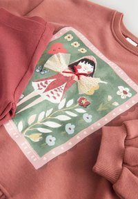 Felpa rosa polverosa per bambini con illustrazione stampata di una ragazza con un cappuccio rosso e decorazioni floreali, a forma di cuore e farfalle.