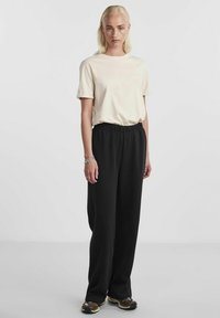 Lys beige bomulls t-skjorte kombinert med svarte vidde bukser med elastisk liv. Modell med flerfargede joggesko med teksturert såle.