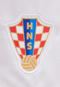 Έμβλημα της Κροατικής ομοσπονδίας χάντμπολ με κόκκινο και λευκό σκακιέρα, μπλε κάθετη λωρίδα με τα γράμματα "HNS" και χρυσή μπάλα χάντμπολ από κάτω.