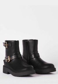 Botines negros hechos de cuero sintético, con dos hebillas doradas, un cierre lateral y una suela de goma gruesa.