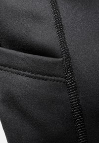 Black athletic fabric with a smooth texture, featuring a small pocket and contrasting stitching along the seam.