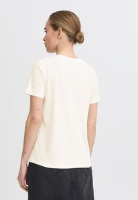 T-shirt à manches courtes, couleur crème, avec un col rond, fabriqué en tissu doux. La vue de dos montre une coupe décontractée et un ourlet arrondi.