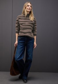 Brązowy sweter z prążkowanym wzorem i wysokim kołnierzem, zestawiony z niebieskimi dżinsami w stylu dzwonów oraz brązową zamszową torbą na ramię. Widoczne czarne buty.
