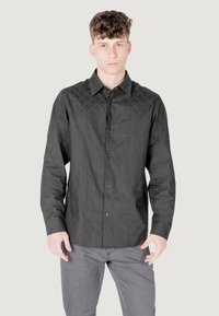 Camicia nera con bottoni, realizzata in tessuto testurizzato, caratterizzata da un motivo geometrico sulle spalle. Include un colletto all'americana e una tasca sul petto.