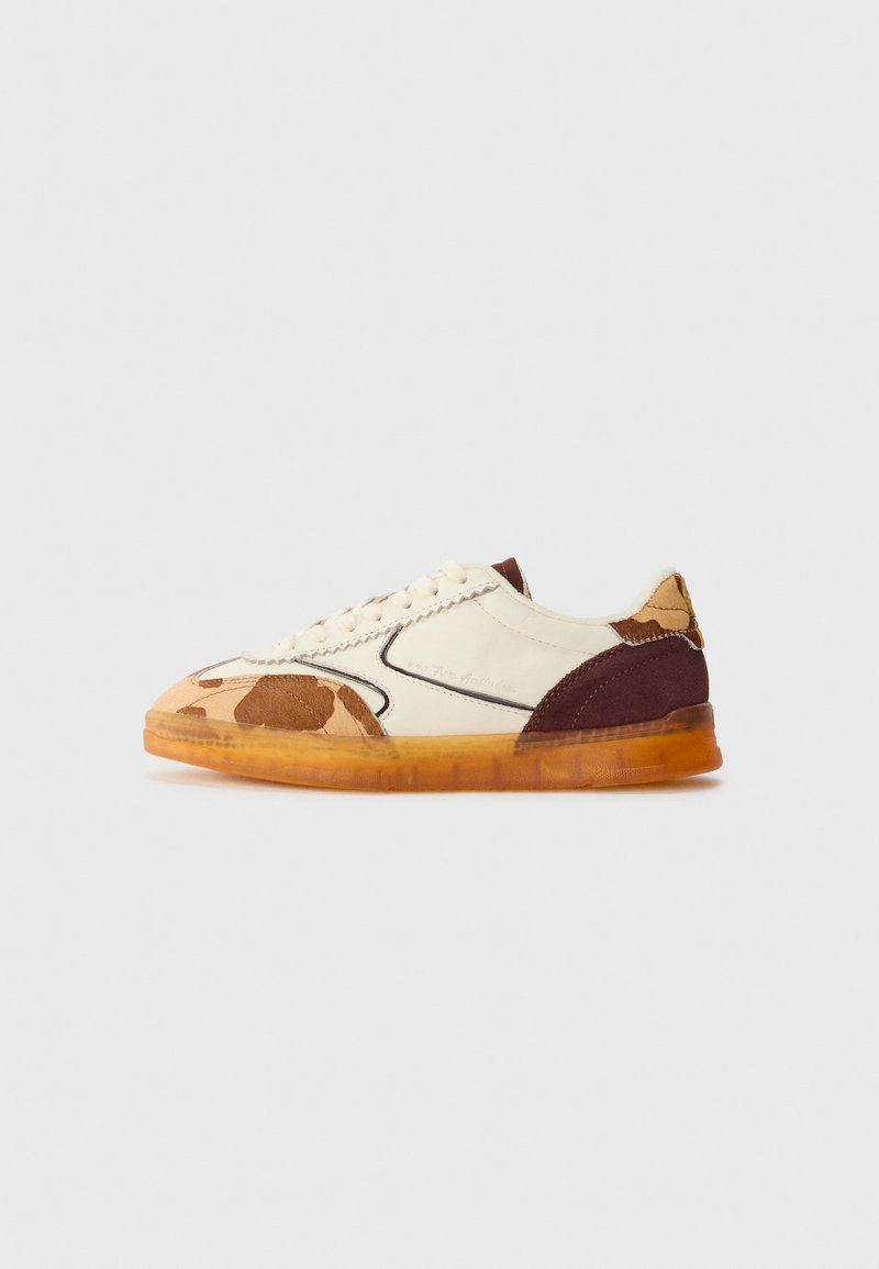 Lave sneakers med kremfarget skinn, brune semskede detaljer, kamuflasje aksenter, og gjennomsiktig ambra gummisåle mot en hvit bakgrunn.
