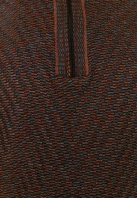 Gestricktes Oberteil mit hohem Kragen und einem Viertelreißverschluss. Das Material hat ein strukturiertes Muster in Braun, Schwarz sowie Anklängen von Blau und Orange.