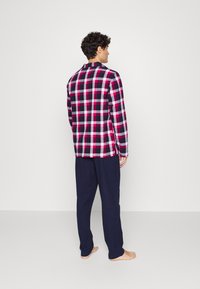 Herren kariertes Hemd in Rot, Schwarz und Weiß, mit langen Ärmeln und Button-Down-Kragen, kombiniert mit dunkelblauen Hosen.