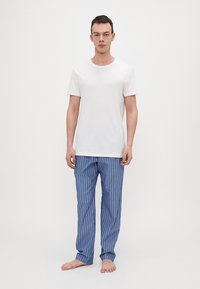 Witte katoenen T-shirt gecombineerd met blauw gestreepte pyjamabroek. De broek heeft verticale strepen in blauw en wit, recht gesneden ontwerp, zonder schoenen.