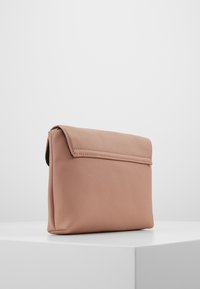 Pudrově růžová kožená kabelka se sklápěcí klopou, hladkou texturou a obdélníkovým tvarem. Minimalistický design bez viditelných kovových prvků.