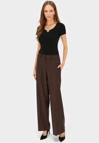 Czarna dopasowana bluzka, brązowe spodnie o szerokich nogawkach z zapięciem na guziki oraz teksturowany naszyjnik. Do tego czarne buty na wysokim obcasie.
