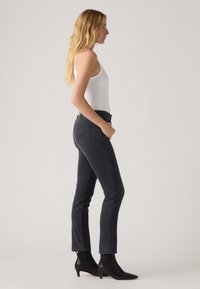 Jeans negros ajustados de cintura alta, con bolsillos delanteros y traseros, combinados con botas de tobillo negras y una camiseta sin mangas blanca ajustada.