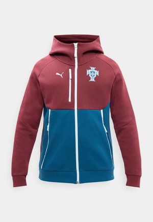 Gewatteerde jas met capuchon en rits, bordeauxrode bovenkant, blauwe onderkant, witte ritsen, Puma-logo op de rechterborst en embleem van de Portugese voetbalbond op de linkerborst.
