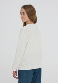 Biały sweter z dzianiny o luźnym kroju, z okrągłym dekoltem i ściągaczami na rękawach. W połączeniu z niebieskimi dżinsami o swobodnym kroju.