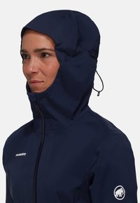 Navy blue waterproof jacket with a fitted hood and adjustable drawstring. Features a zip closure and a logo on the left sleeve.