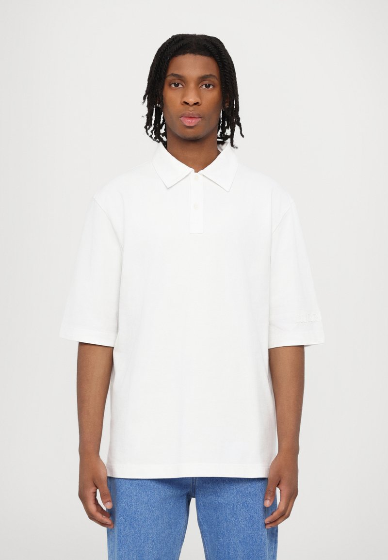 White polo shirt with short sleeves, folded collar, and button placket, paired with light blue denim jeans. Smooth cotton texture, no patterns.