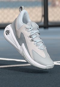 Chaussure de sport gris clair avec un dessus en maille et en daim, design à lacets, semelle texturée et marquage bien visible sur le côté.