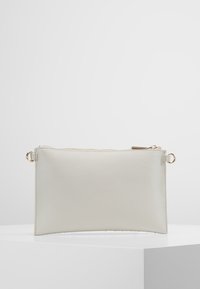 Pochette en cuir blanc à la texture lisse, de forme rectangulaire, avec une fermeture éclair dorée. Elle comporte deux anneaux métalliques sur les côtés.